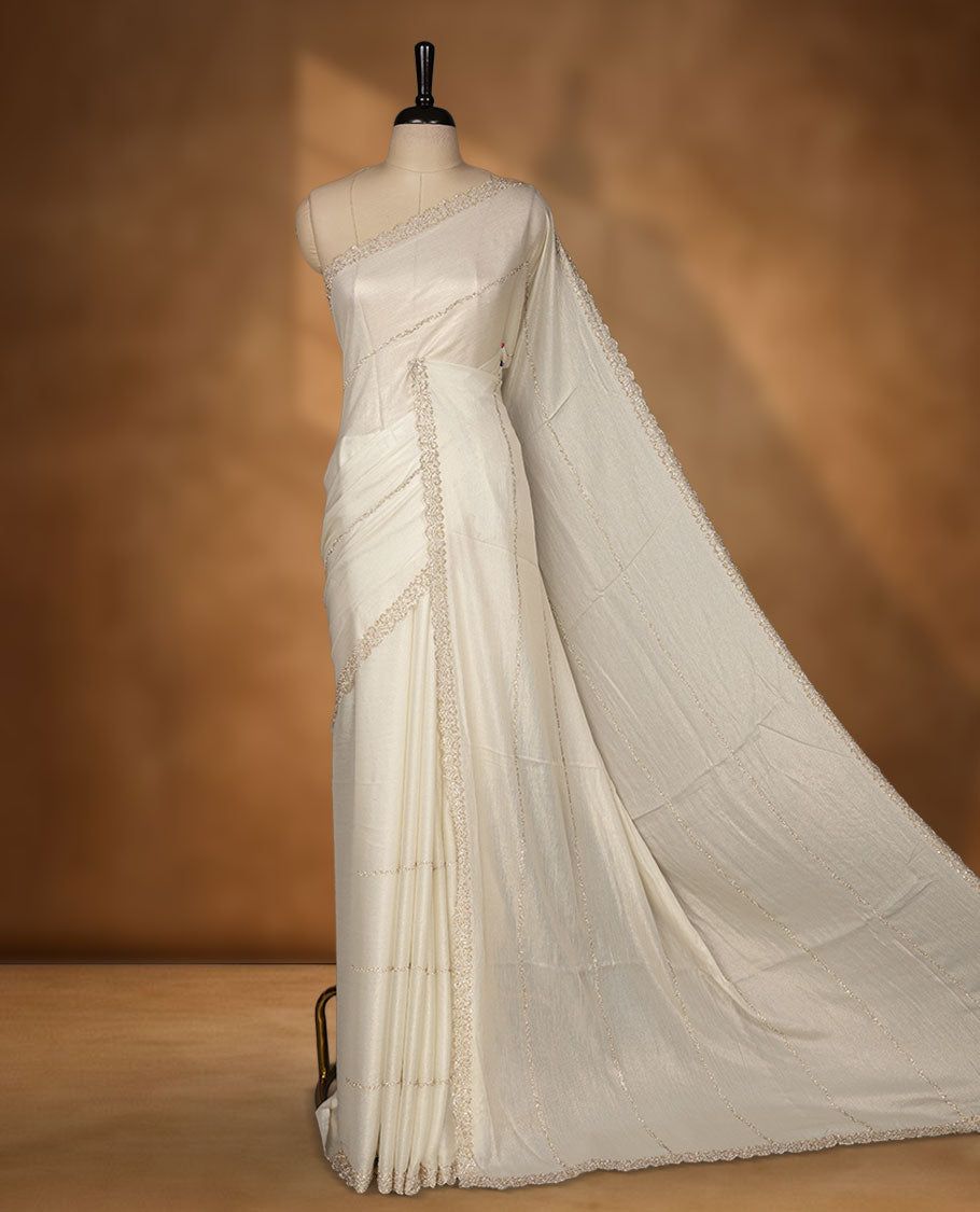 Pastel Cream Colour shimmer fancy saree adorned with scattered gold stone buttas all over the body, paired with a delicate stone worked border and matching blouse
