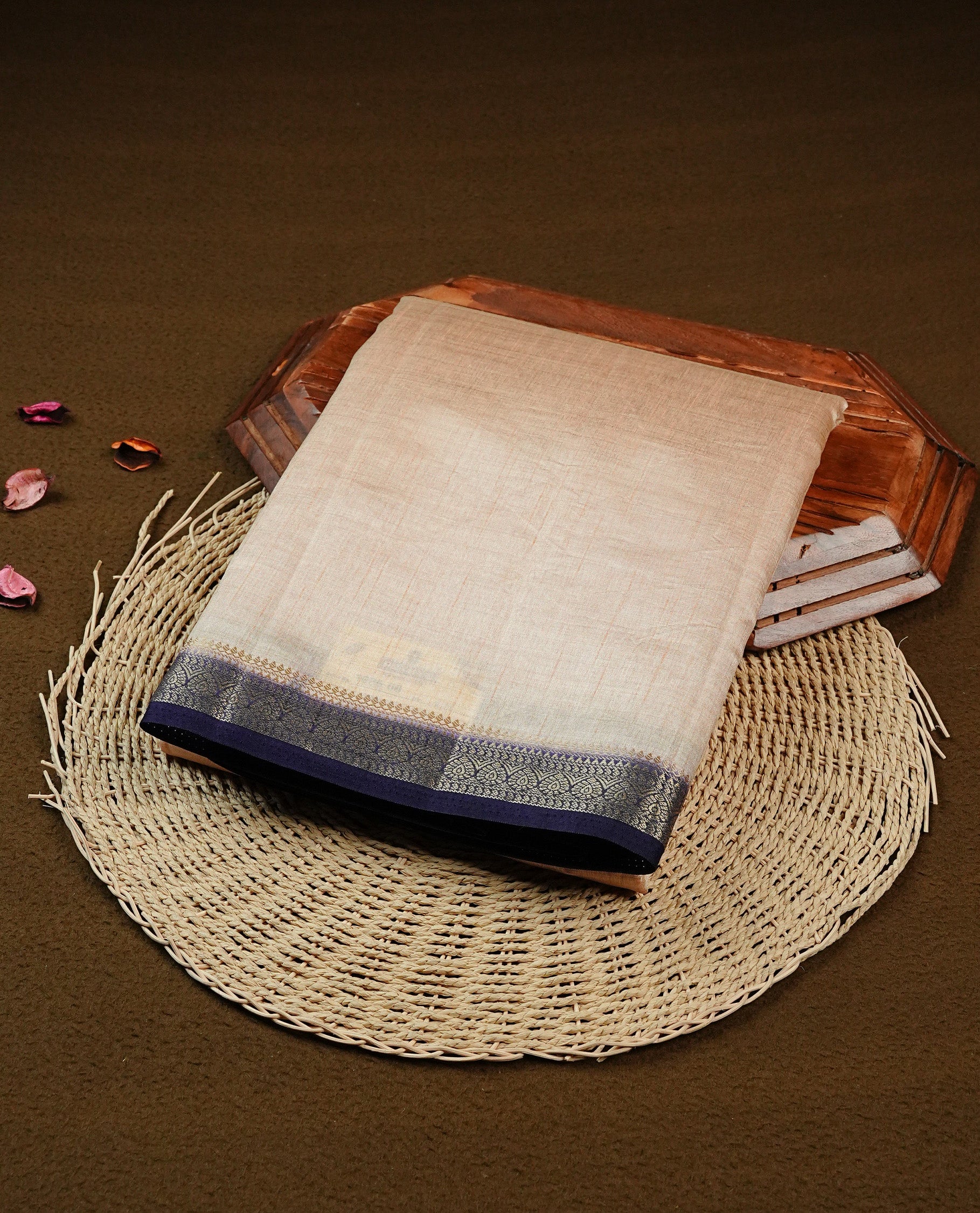 Cream colour Semi Tussar silk saree featuring an elegant plain body, accentuated by a contrast Navy blue border adorned with intricate gold zari work, paired with a matching blouse piece.