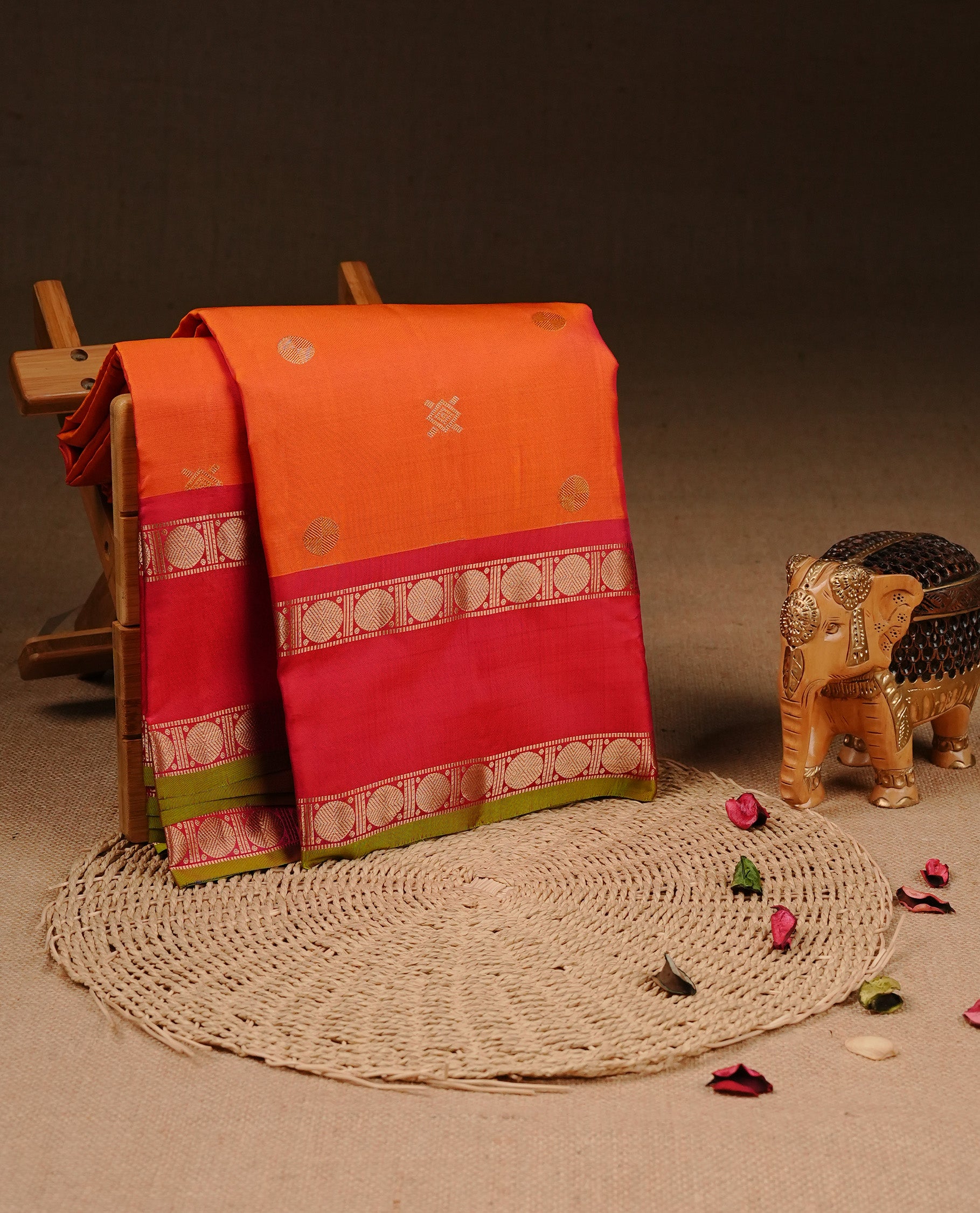 Orange colour Traditional Kancheepuram silk saree featuring gold zari motifs on body, enhanced with contrast Red with traditional with green piping border, paired with matching blouse piece.
