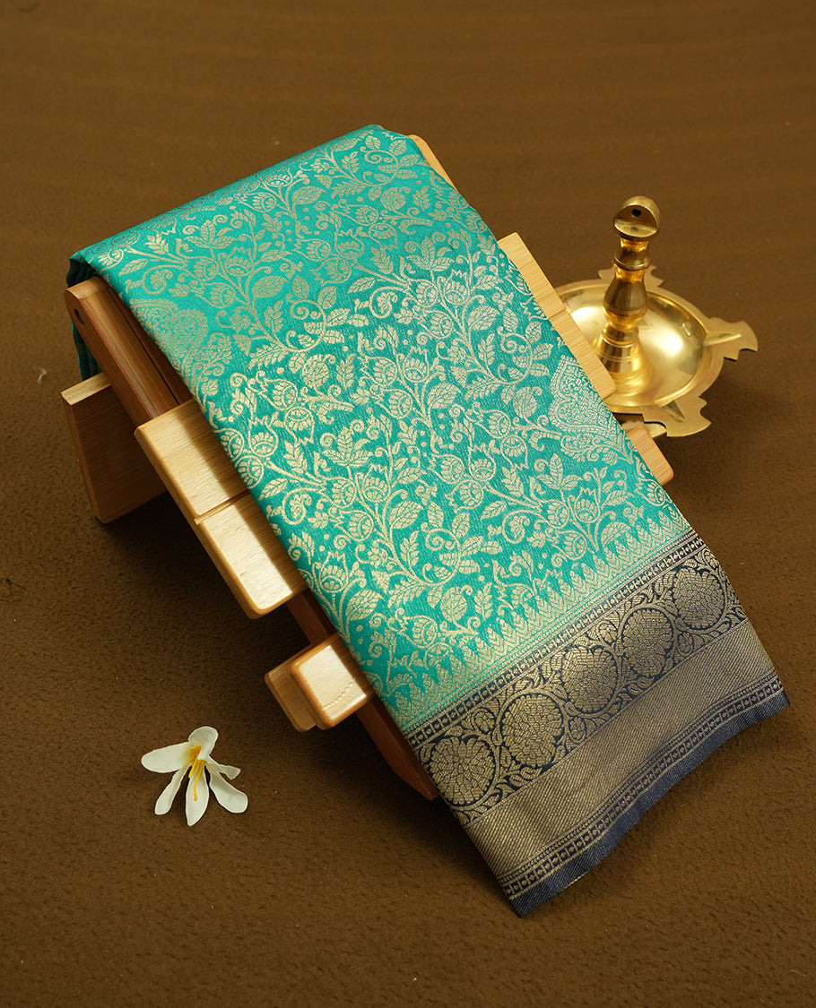 Aqua green colour semi silk brocade saree featuring intricate Gold Floral kodi patterns across the body, complemented by a contract dark blue colour woven border and pallu, paired with a matching blouse.