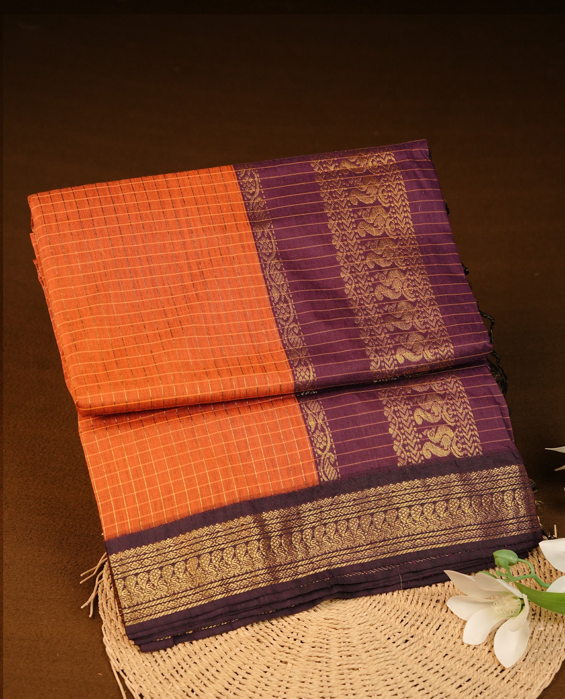 Orange colour Kalyani cotton saree featuring Gold zari check pattern on body, complemented by Contrast Purple colour with grand gold zari border & pallu, matching blouse piece