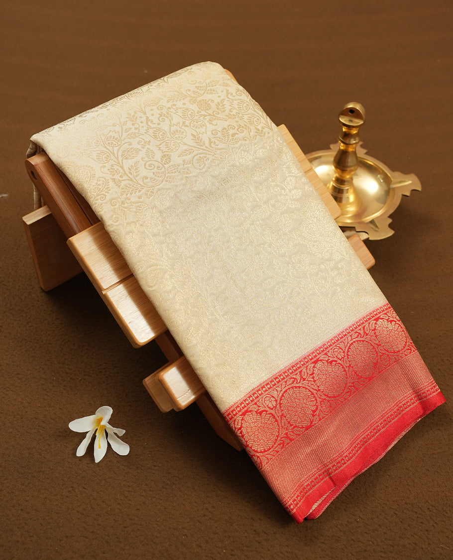 Cream colour semi silk brocade saree featuring intricate Gold floral kodi patterns across the body, complemented by a Contrast rich red colour woven border and pallu, paired with a matching blouse.