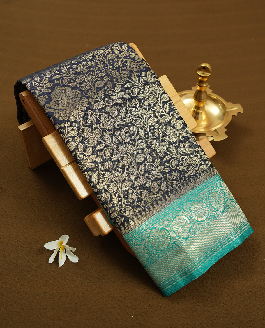 Dark Blue colour semi silk brocade saree featuring intricate Gold Floarl kodi patterns across the body, complemented by a contrast rich Aqua green colour woven border and pallu, paired with a matching blouse.