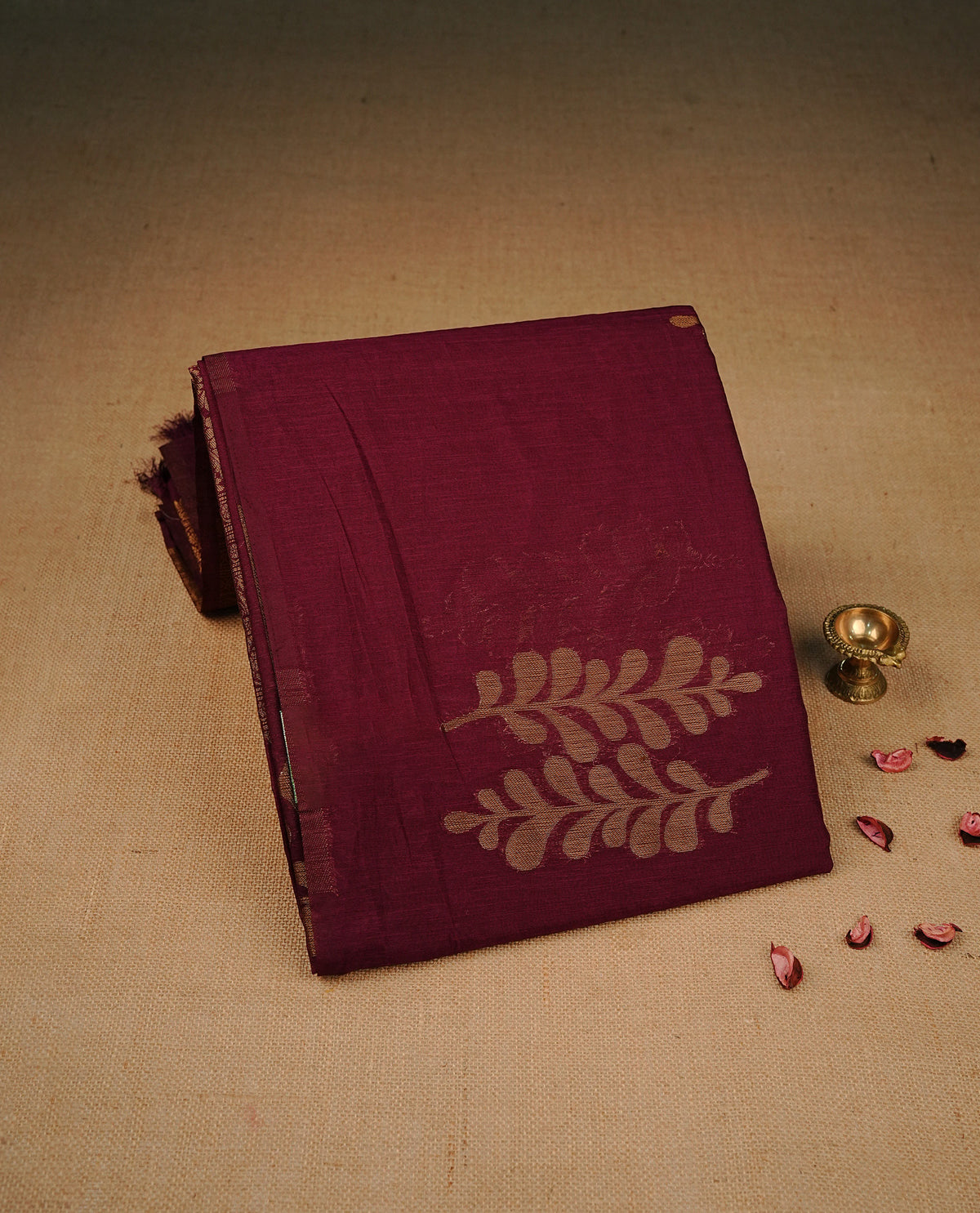 Wine colour semi silk saree featuring Gold zari Leaf pattern on body, complemented by contrast Rust Orange colour with Gold zari border, comes with matching blouse piece.
