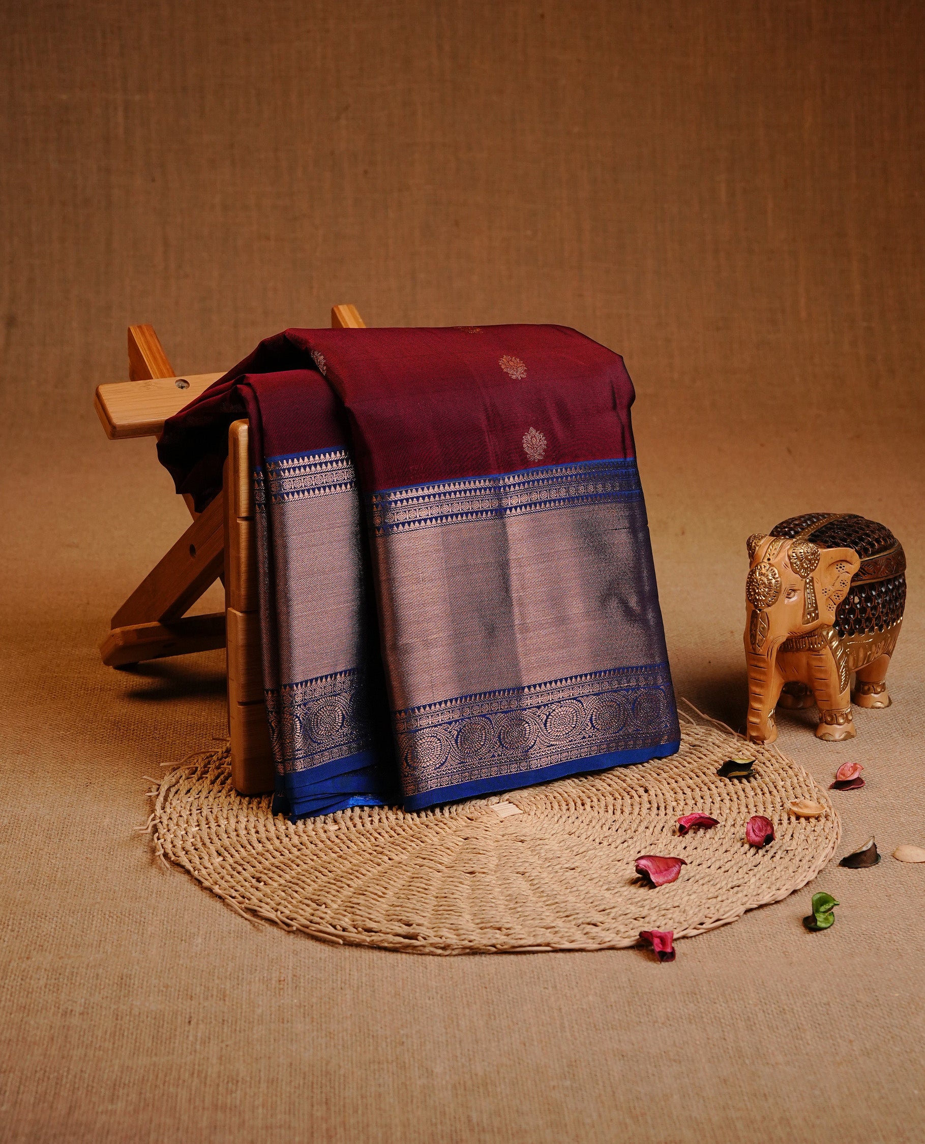 Maroon Colour Traditional Kancheepuram Silk Saree Featuring Gold Zari Floral Motifs on the Body, Complemented by a Contrast Blue Colour Copper Zari Traditional Border and Pallu, Paired with a Matching Blouse .