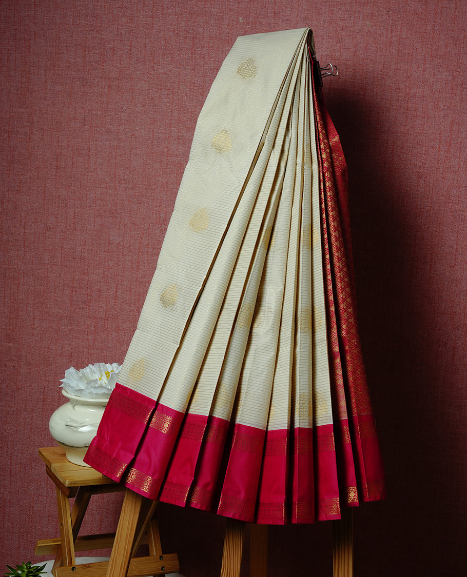Cream coloured soft silk saree featuring gold zari stripes and motifs across the body, enhanced with a contrast Magenta border and pallu, paired with a matching contrast blouse piece.