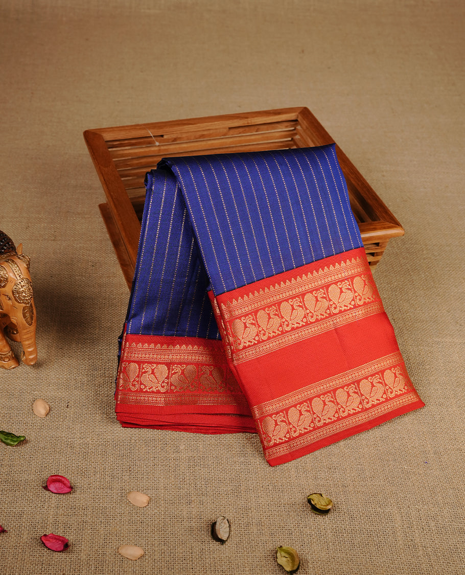 Navy blue colour traditional kancheepuram silk saree featuring gold zari strpies on body, complemented by contrast red colour with gold zari traditional border, paired with matching blouse piece.