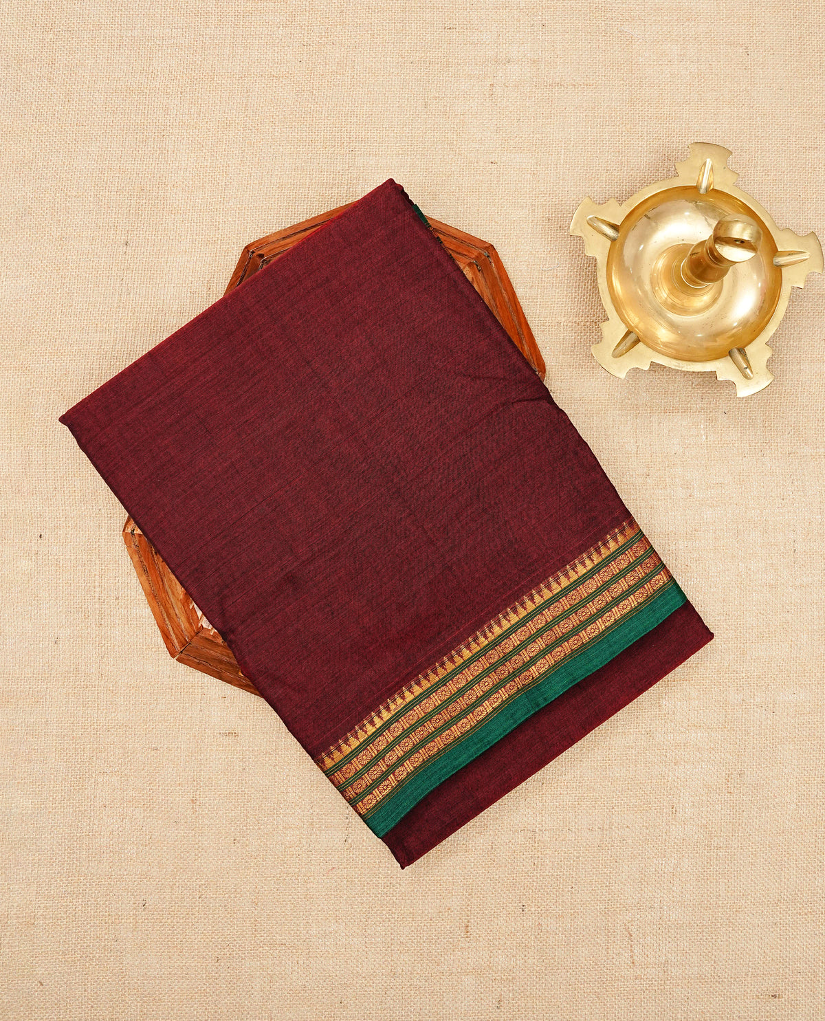Maroon colour Narayanapattu cotton saree with a plain body, complemented by a Green colour with Gold Zari border & contrast pallu, paired with a matching blouse piece