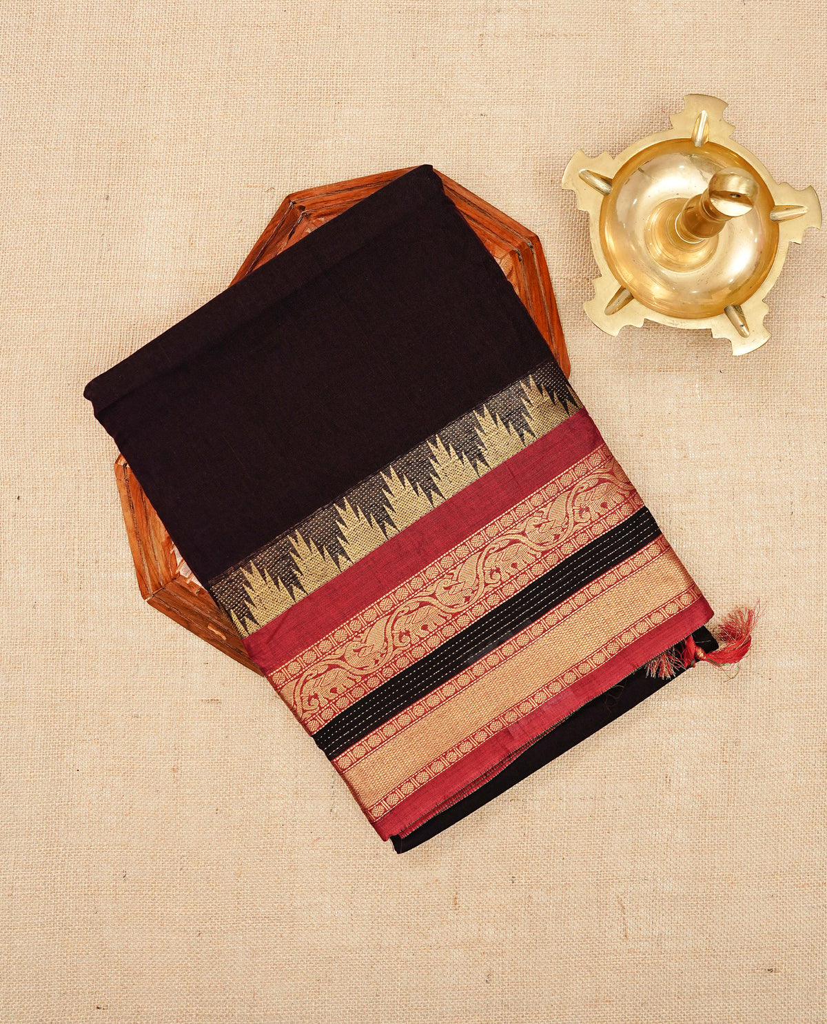 Dark Brown colour Narayanapattu cotton saree with a plain body, complemented by a red colour with Gold Zari & temple designed border & contrast pallu, paired with a matching blouse piece.