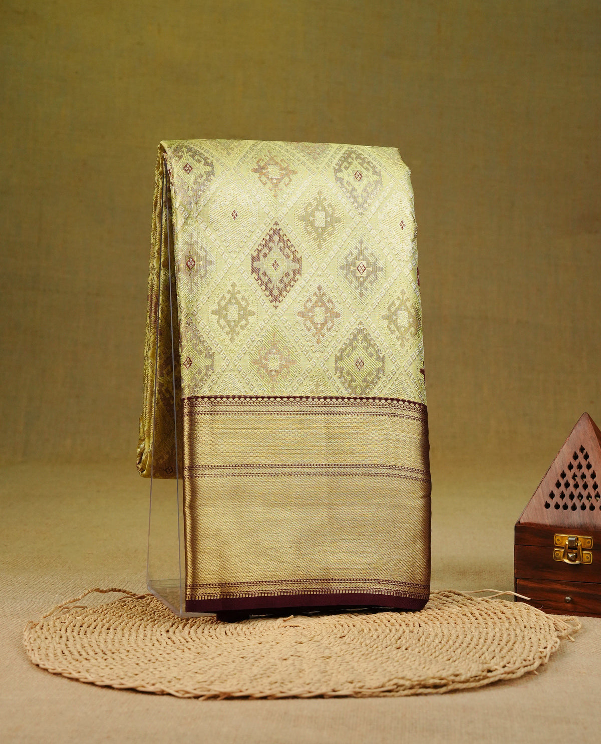 Yellowish gold colour pure tissue silk saree featuring an elegant chocolate toned geometric pattern across the body, complemented by a dark chocolate traditional border. Comes with a matching blouse piece.