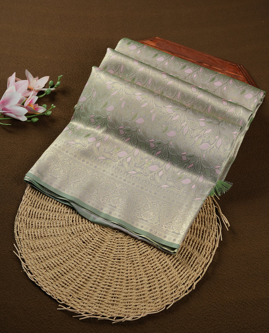 Pastel green colour semi soft silk saree featuring an all-over woven leaf pattern in gold colour, finished with a matching border adorned with detailed paisley and floral motifs, and a matching blouse piece.