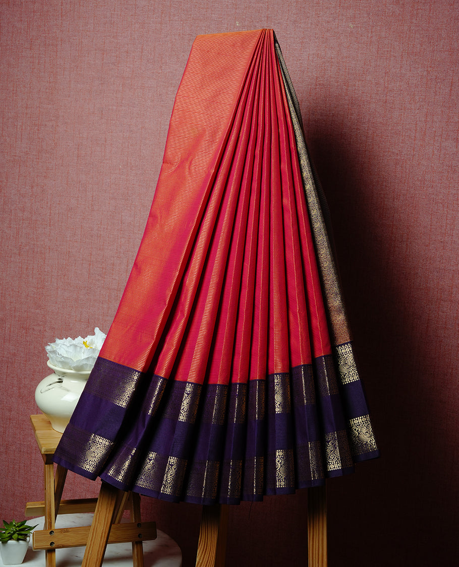 Rust orange coloured soft silk saree featuring gold zari stripes and motifs across the body, enhanced with a contrast Purple border and pallu, paired with a matching contrast blouse piece.