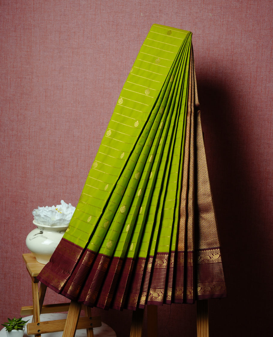 Lemon coloured soft silk saree featuring gold zari stripes and motifs across the body, enhanced with a contrast Maroon border and pallu, paired with a matching contrast blouse piece.