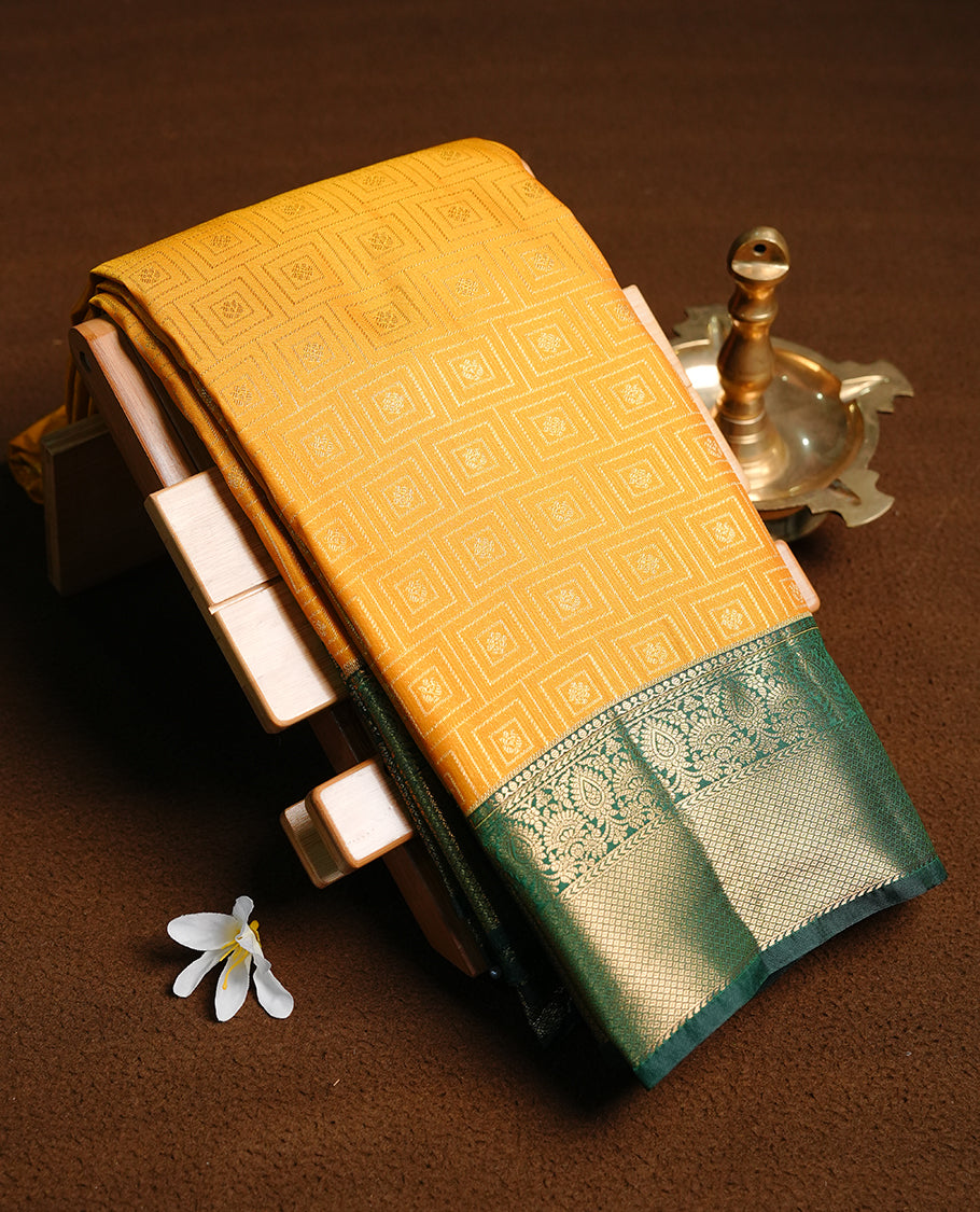 Mustard colour semi wedding saree featuring gold zari motif on check pattern on body, complemented by contrast green with traditional border, paired with matching blouse piece.