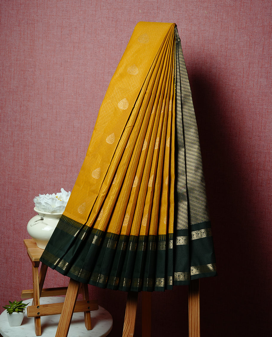 Mustard coloured soft silk saree featuring gold zari stripes and motifs across the body, enhanced with a contrast Dark green border and pallu, paired with a matching contrast blouse piece.