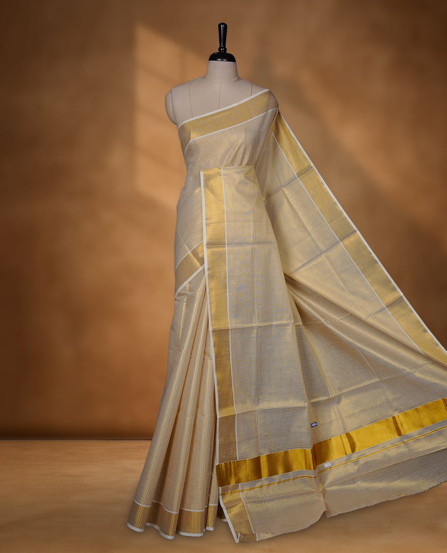 Off-white colour tissue Kerala saree with a subtle gold-toned checkered body, finished with a classic gold kasavu border along the edges and pallu, paired with a matching blouse.