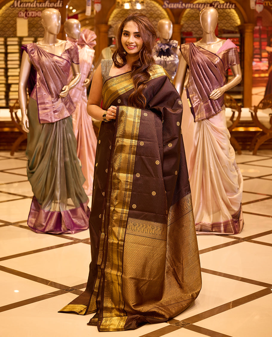 Graceful deep chocolate brown colour Kancheepuram silk saree adorned with delicate gold zari motifs across the body, beautifully finished with a broad traditional gold zari border, exuding timeless elegance and paired with a matching blouse piece