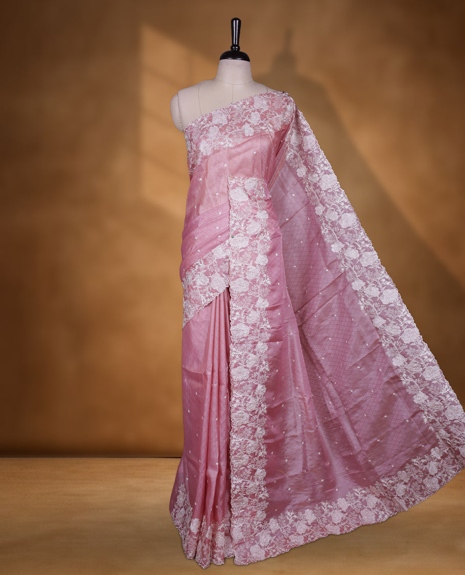 Pink colour organza designer saree featuring a subtle self patterned body and an intricately scalloped floral thread embroidered border all around, complemented by a coordinating embroidered pallu and paired with a matching blouse.