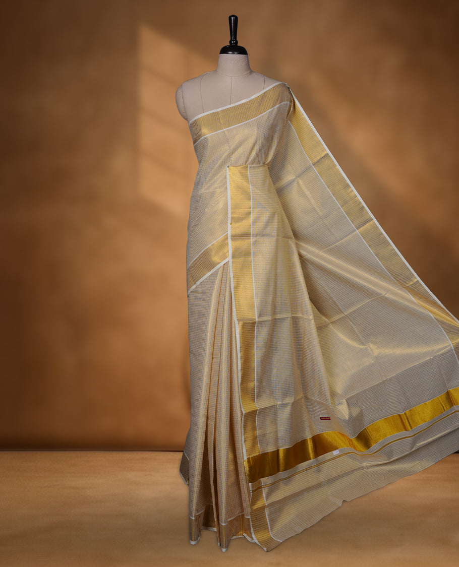 Off-white colour tissue Kerala saree featuring subtle gold checks throughout the body, finished with a classic gold kasavu border and a graceful pallu, paired with a matching blouse.