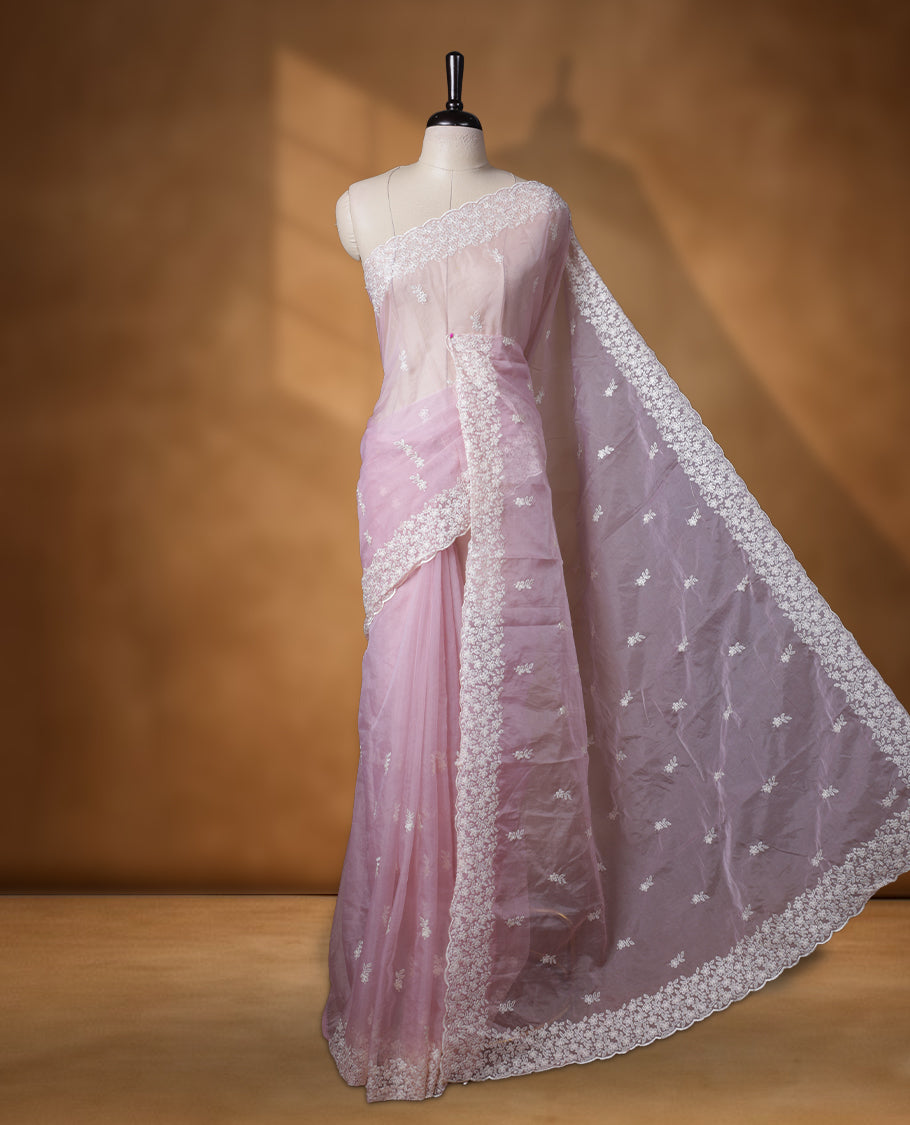 Light Pink colour organza designer saree featuring a subtle self patterned body and an intricately scalloped floral thread embroidered border all around, complemented by a coordinating embroidered pallu and paired with a matching blouse.