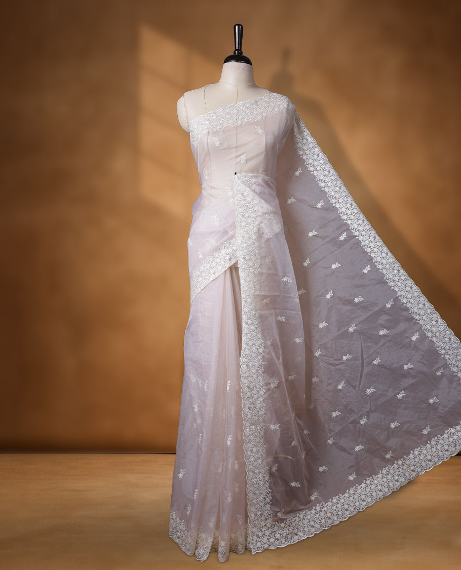 Cream colour organza designer saree featuring a subtle self patterned body and an intricately scalloped floral thread embroidered border all around, complemented by a coordinating embroidered pallu and paired with a matching blouse.