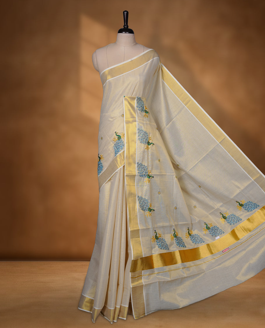 Off-white Kerala saree featuring a classic gold kasavu border, highlighted with graceful blue peacock motifs across the body and pallu, and paired with a matching blouse.