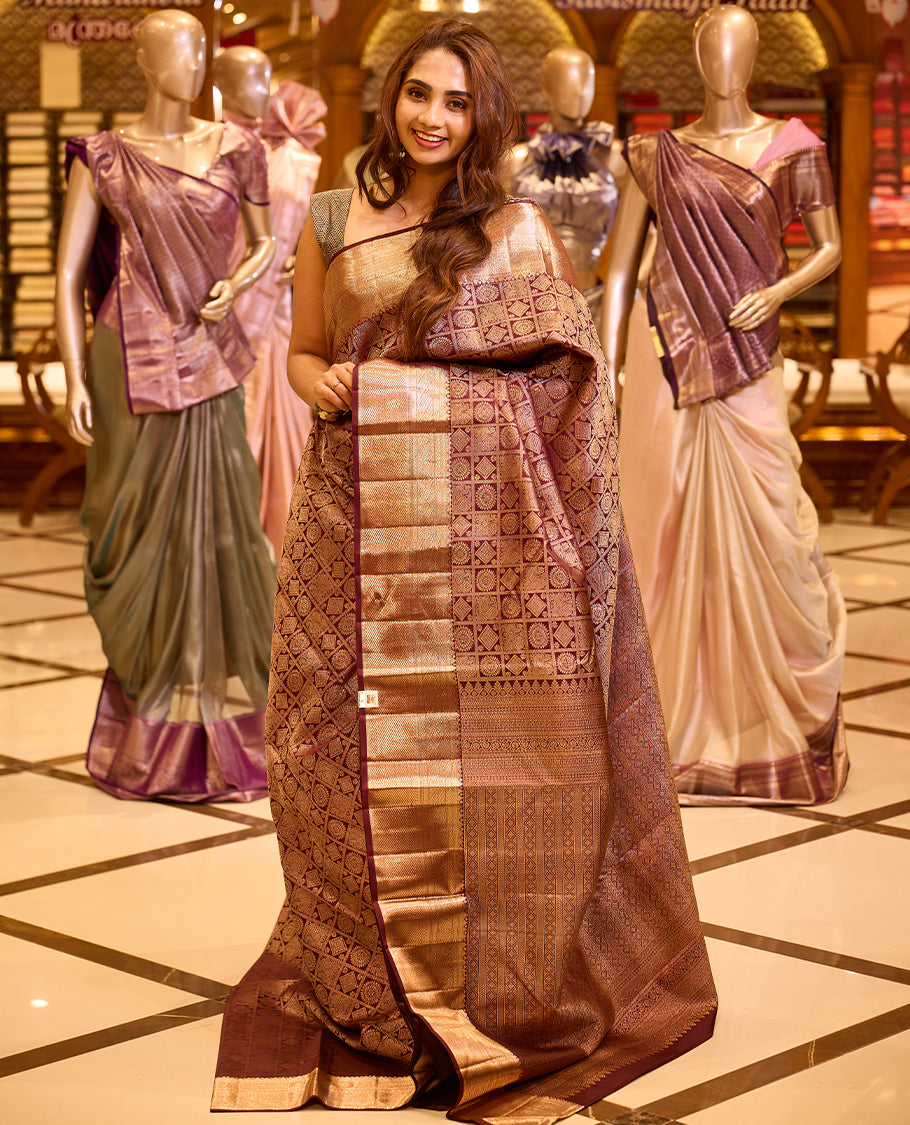 Elegant wine brown colour Kancheepuram silk saree adorned with an all over rich geometric zari weave, beautifully complemented by a broad traditional gold zari border and paired with a matching blouse piece