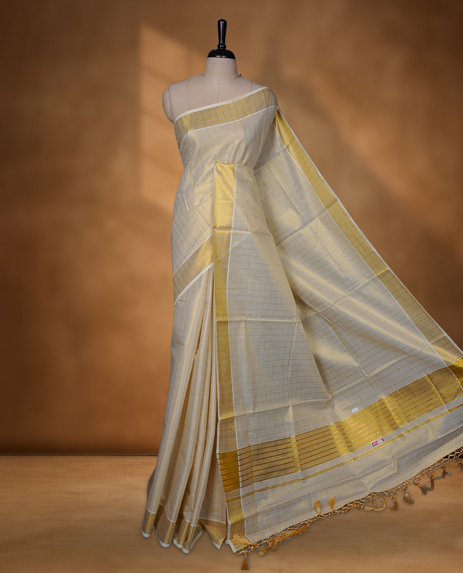 Off-white colour tissue Kerala saree with subtle gold checks across the body, finished with a traditional striped gold kasavu border and delicate tassel detailing on the pallu, paired with a matching blouse.