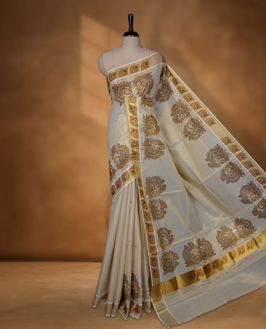 Off-white colour tissue Kerala saree with an elegant gold kasavu border, adorned with antique gold peacock and paisley motifs across the body and pallu, paired with a matching blouse.