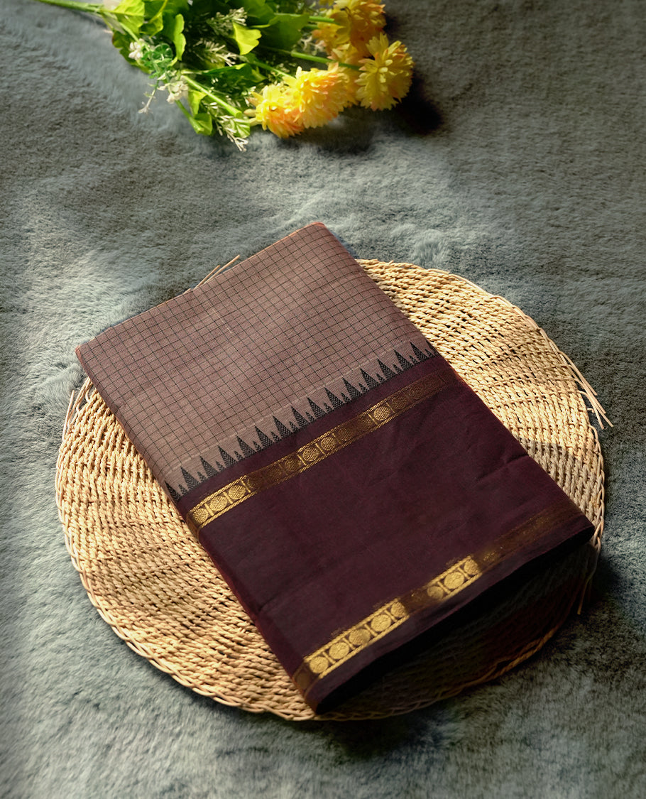 Brown colour checked Chettinad cotton saree featuring intricate black checks on the body, enhanced with golden zari borders and temple motifs & Comes with a matching blouse piece for a traditional look.