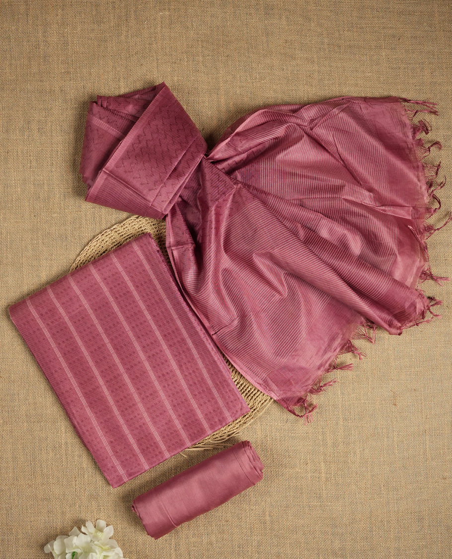 Dusty rose colour tussar suit material featuring a subtle self woven pattern and vertical lines on the body, paired with a lightweight matching dupatta with tassel edges and a plain bottom piece.