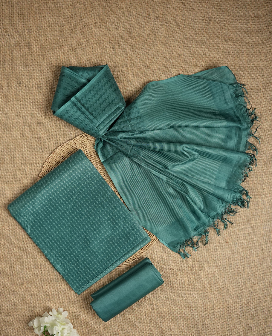 Teal blue colour tussar suit material featuring a subtle self woven textured body, paired with a soft striped dupatta detailed with tassel edges and a matching bottom piece.