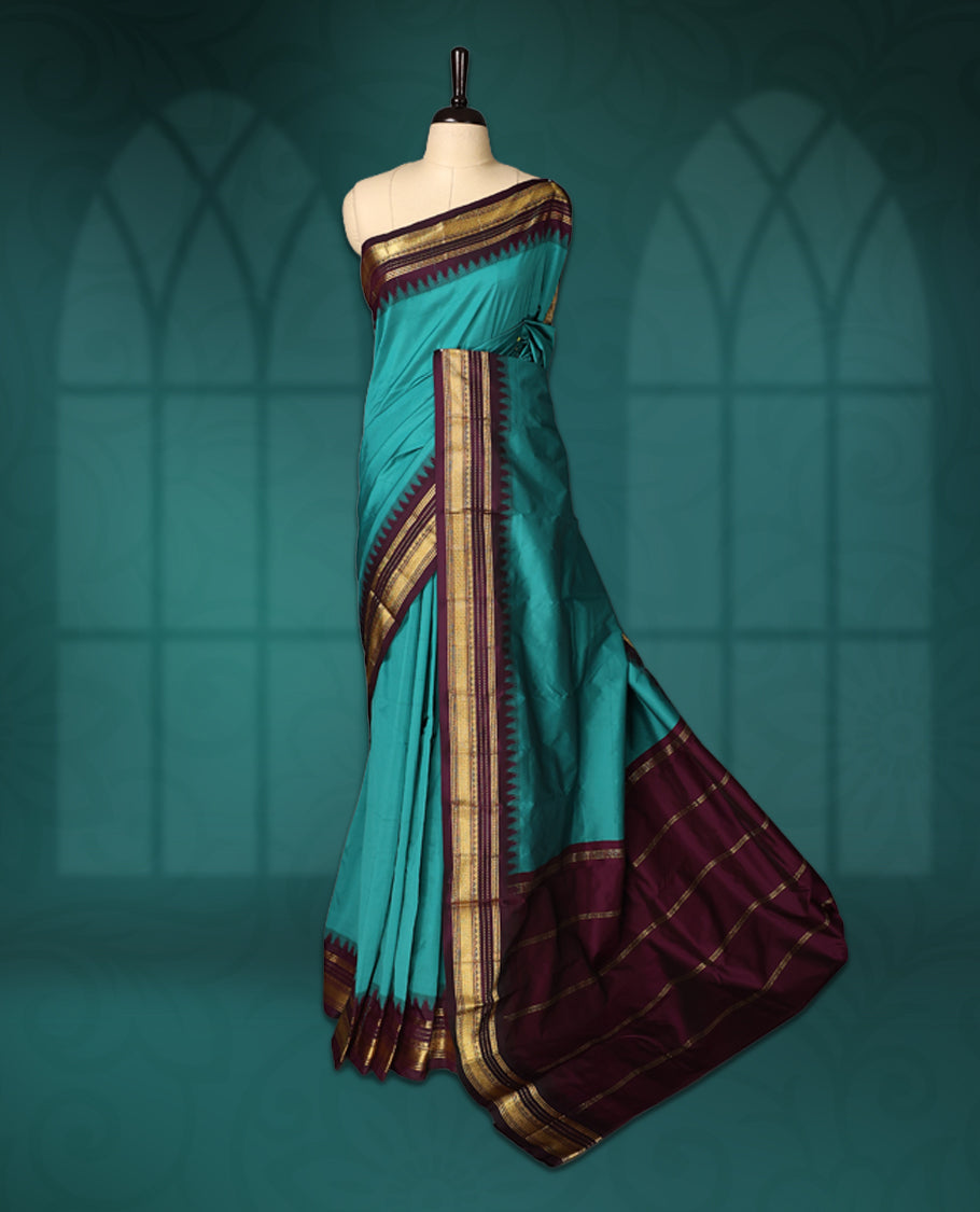 Peacock green semi silk saree with plain body, vibrant deep violet pallu and matching violet border adorned with golden zari, accented with temple motifs along the edges, Paired with a matching blouse, perfect for festive occasions.