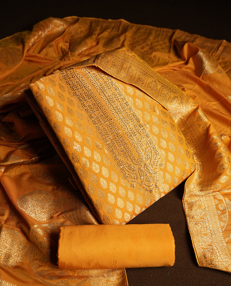 Mustard yellow colour churidar material featuring small golden stone work on the neckline, adorned with zari leaf motifs all over & Comes with a rich zari woven dupatta and matching plain bottom.