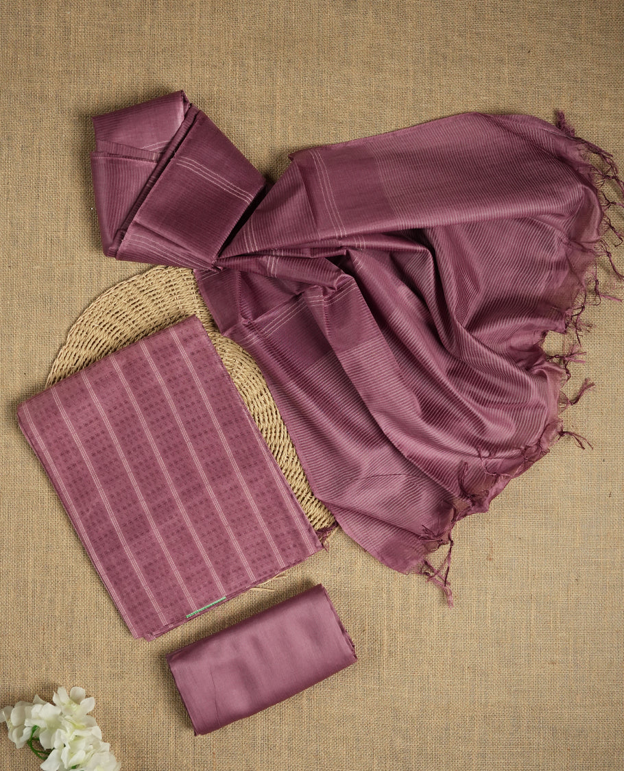 Mauve colour tussar suit material featuring a subtle self woven pattern and vertical lines on the body, paired with a lightweight matching dupatta with tassel edges and a plain bottom piece.