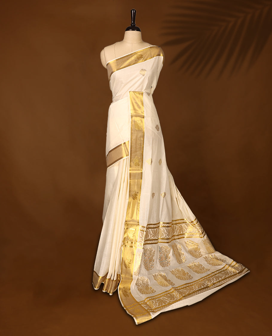 Elegant off white colour cotton Kerala saree embellished with golden buttas across the body and an ornate golden zari border and pallu featuring intricate motifs & A perfect traditional pick, paired with a matching blouse piece.