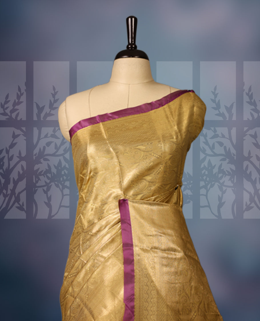 Golden semi silk brocade saree with intricate self brocade work across the body, paired with a rich contrast violet border and matching pallu. Includes a coordinating blouse for an elegant traditional look.
