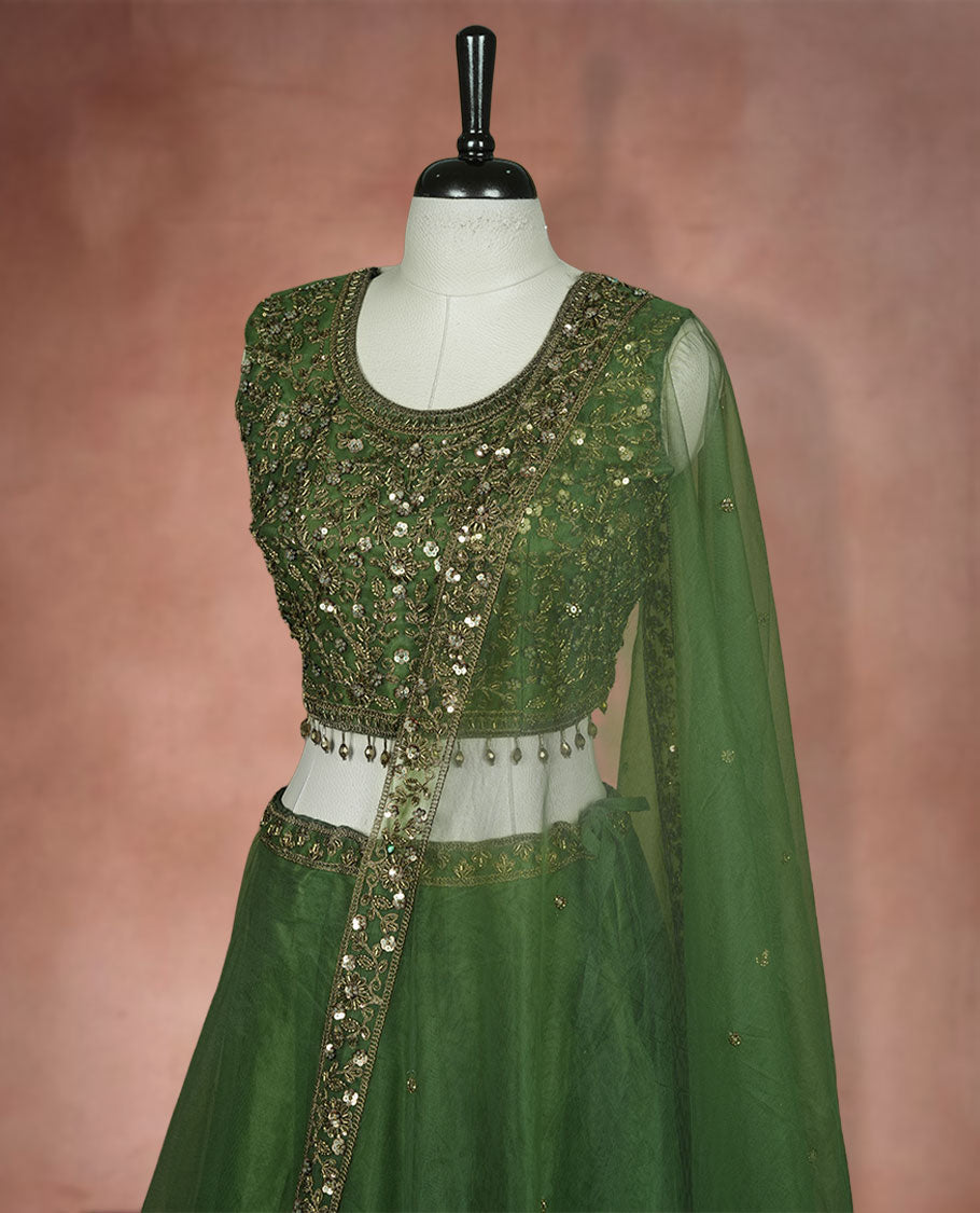 Olive green colour lehenga set with stitched sleeveless Antique thread embroidered & beats worked blouse featuring sheer neckline, matching stitched flared lehenga, and plain sheer dupatta.