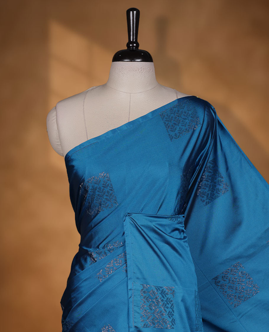 Ocean Blue colour semi soft silk saree adorned with delicate woven floral in square motifs on the body, complemented by a Self colour woven pallu with intricate detailing and tassel accents without border & Comes with a matching blouse piece.
