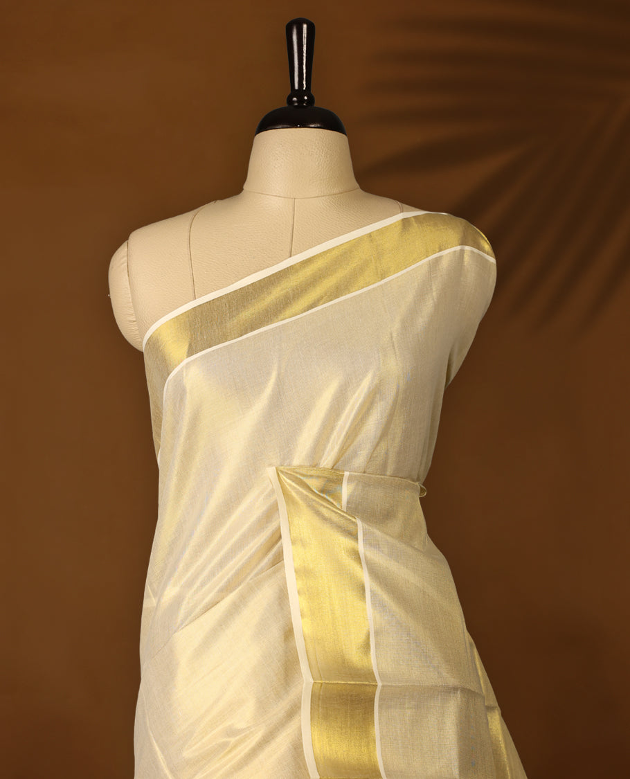 Elegant off white Kerala saree in tissue, featuring a plain body, shimmering gold zari kasavu border, and rich pallu with intricate zari patterns. Comes with a matching blouse, perfect for festive occasions.