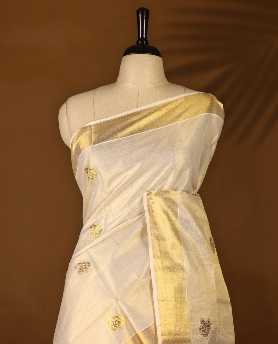 Elegant off white colour tissue Kerala saree with gold zari buttas, broad kasavu border, and richly woven traditional pallu. Crafted in cotton and paired with a matching blouse, perfect for festive and traditional occasions.