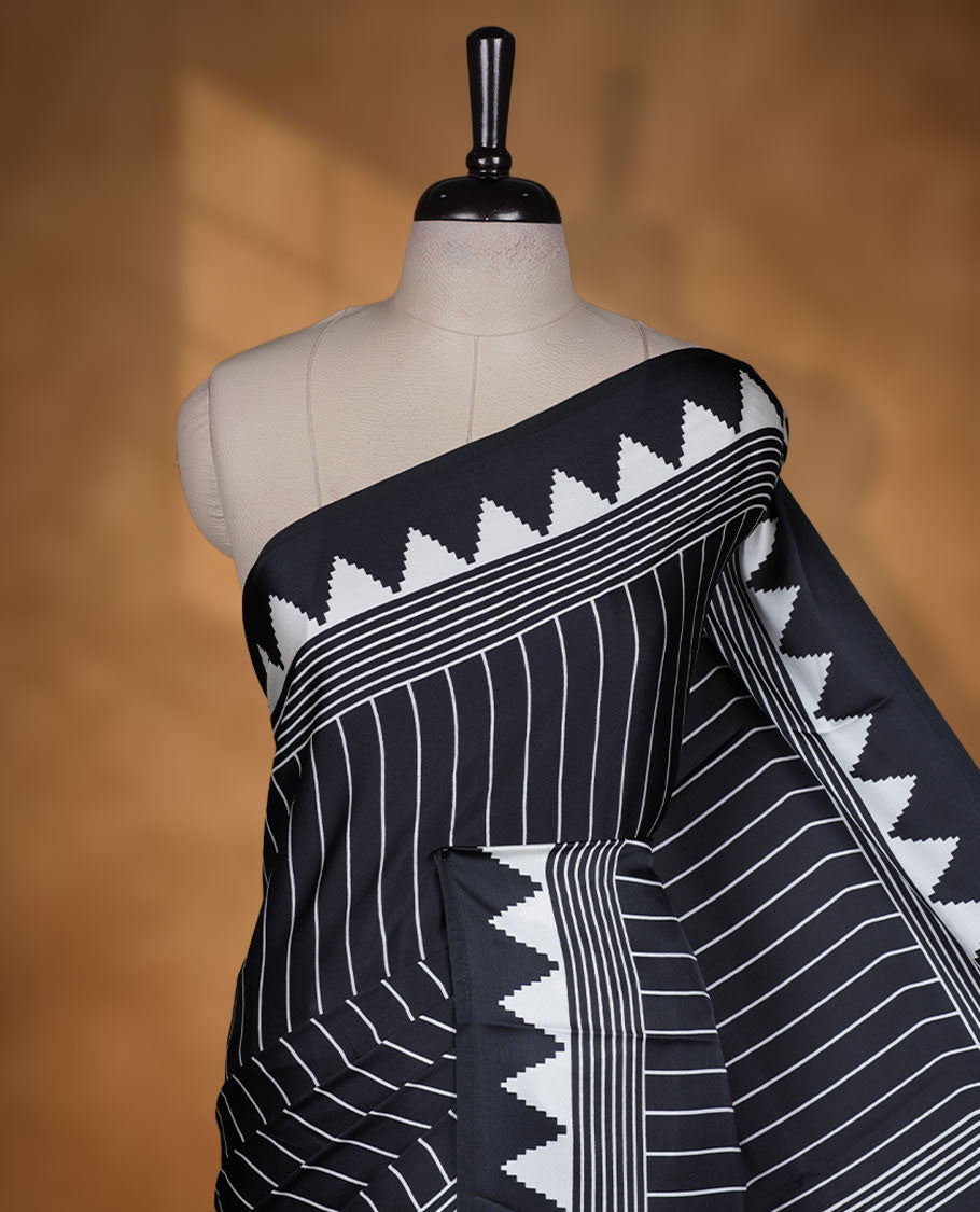 Black colour semi modal saree featuring white colour geometric borders and fine stripe detailing, finished with an oversized circular motif on the pallu, paired with a matching printed blouse.