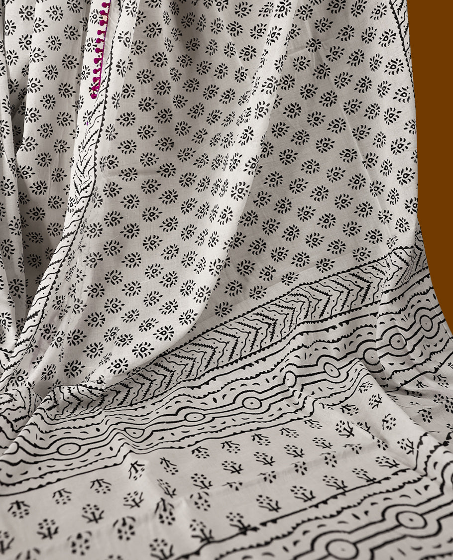 White cotton saree features intricate black handblock prints, a beautifully detailed border with pink piping and Self Coloured Blouse