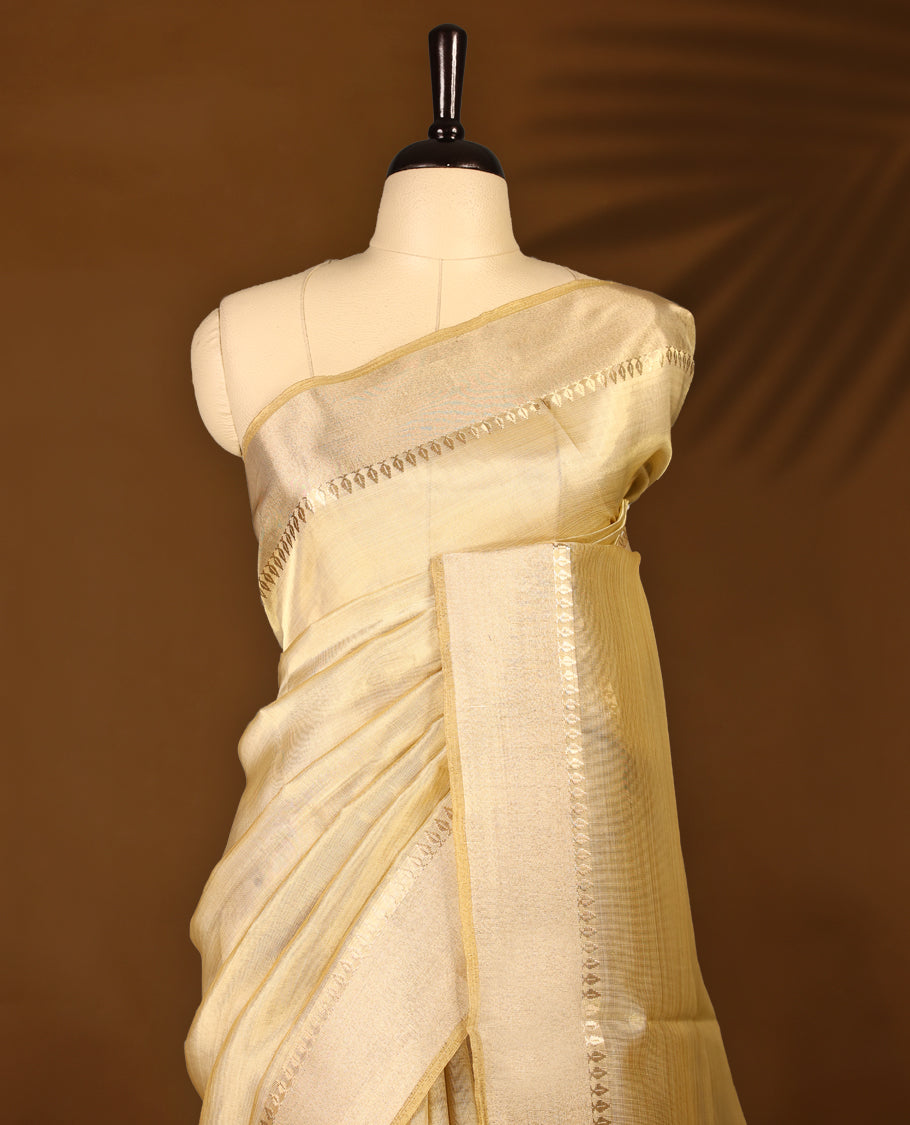 Light gold colour Organza Kerala saree featuring a sheer, luminous body with a soft golden stripes, highlighted by a sleek zari border, Minimal and elegant, it is paired gracefully with a matching blouse piece.