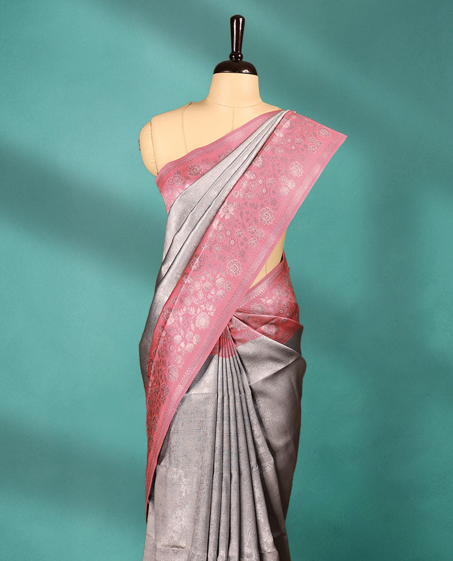 Silver coloured semi silk saree featuring a self coloured floral jaal design on the body, paired with an onion coloured border and matching blouse.