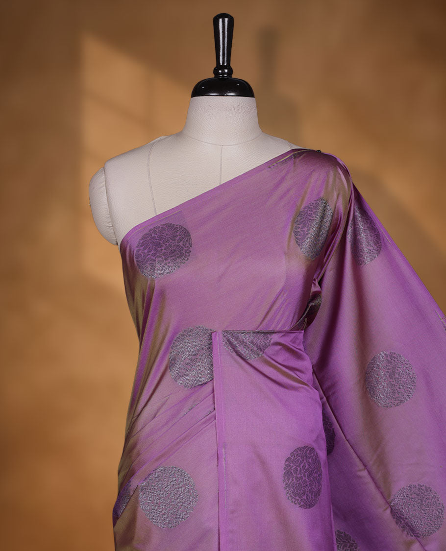 Lavender colour semi soft silk saree adorned with delicate woven floral chakkram motifs on the body, complemented by a contrast purple colour woven pallu with intricate detailing and tassel accents without border & Comes with a matching blouse piece.