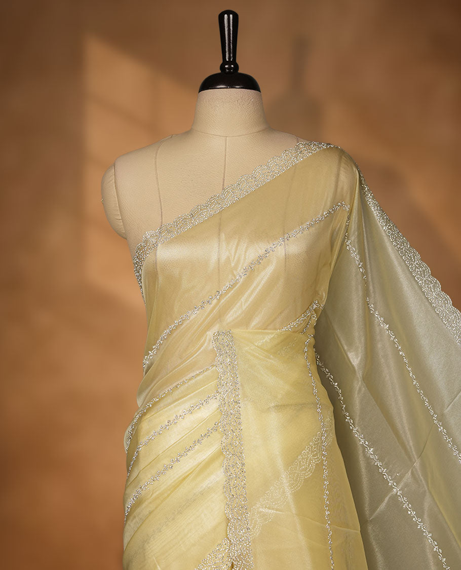 Pale yellow colour net shimmer fancy saree adorned with scattered white stone buttas all over the body, paired with a delicate stone worked border and matching blouse.