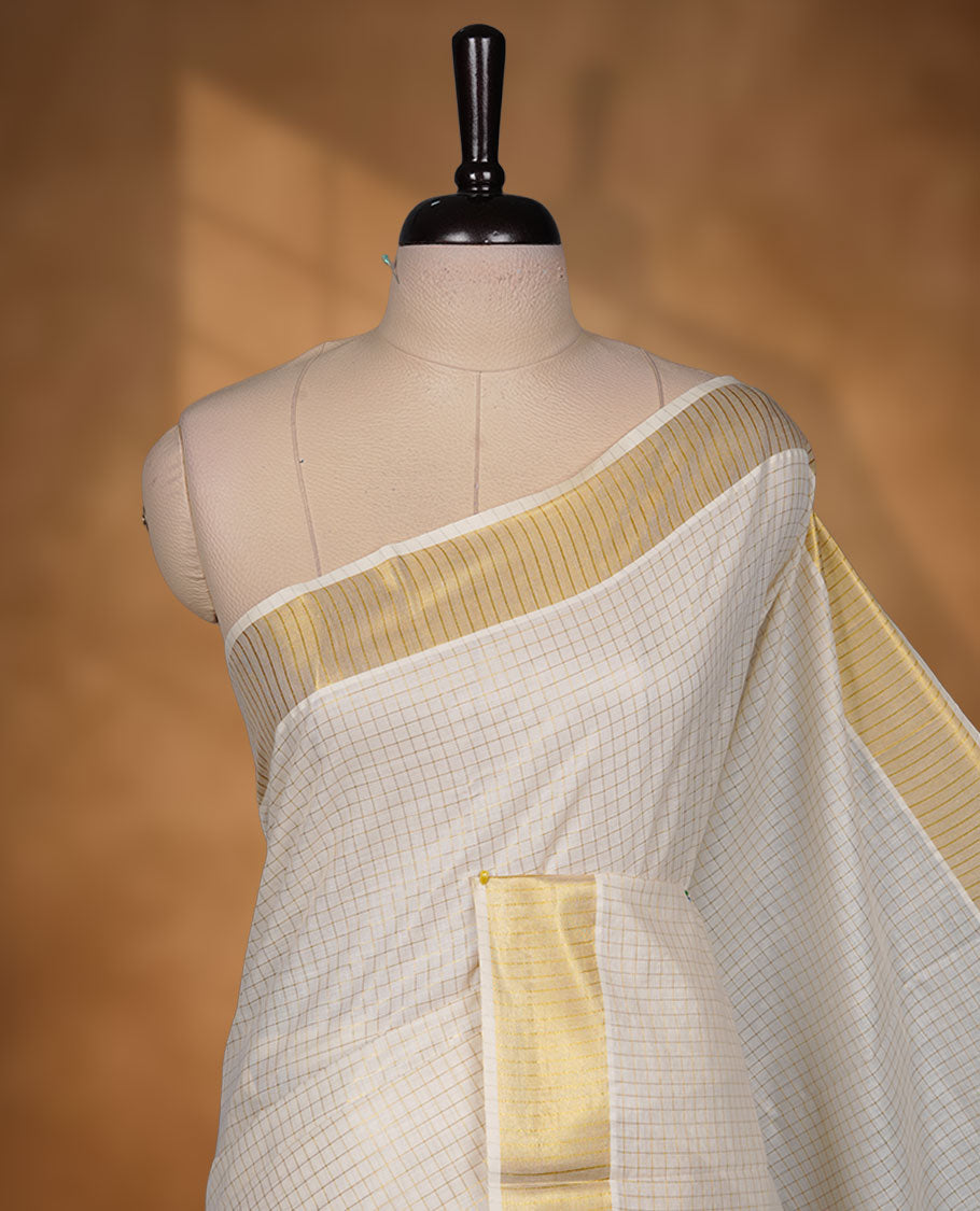 Off-white colour cotton Kerala saree featuring a subtle golden checkered body, highlighted with a classic gold kasavu border accented by fine red lines, and finished with a matching cotton blouse.