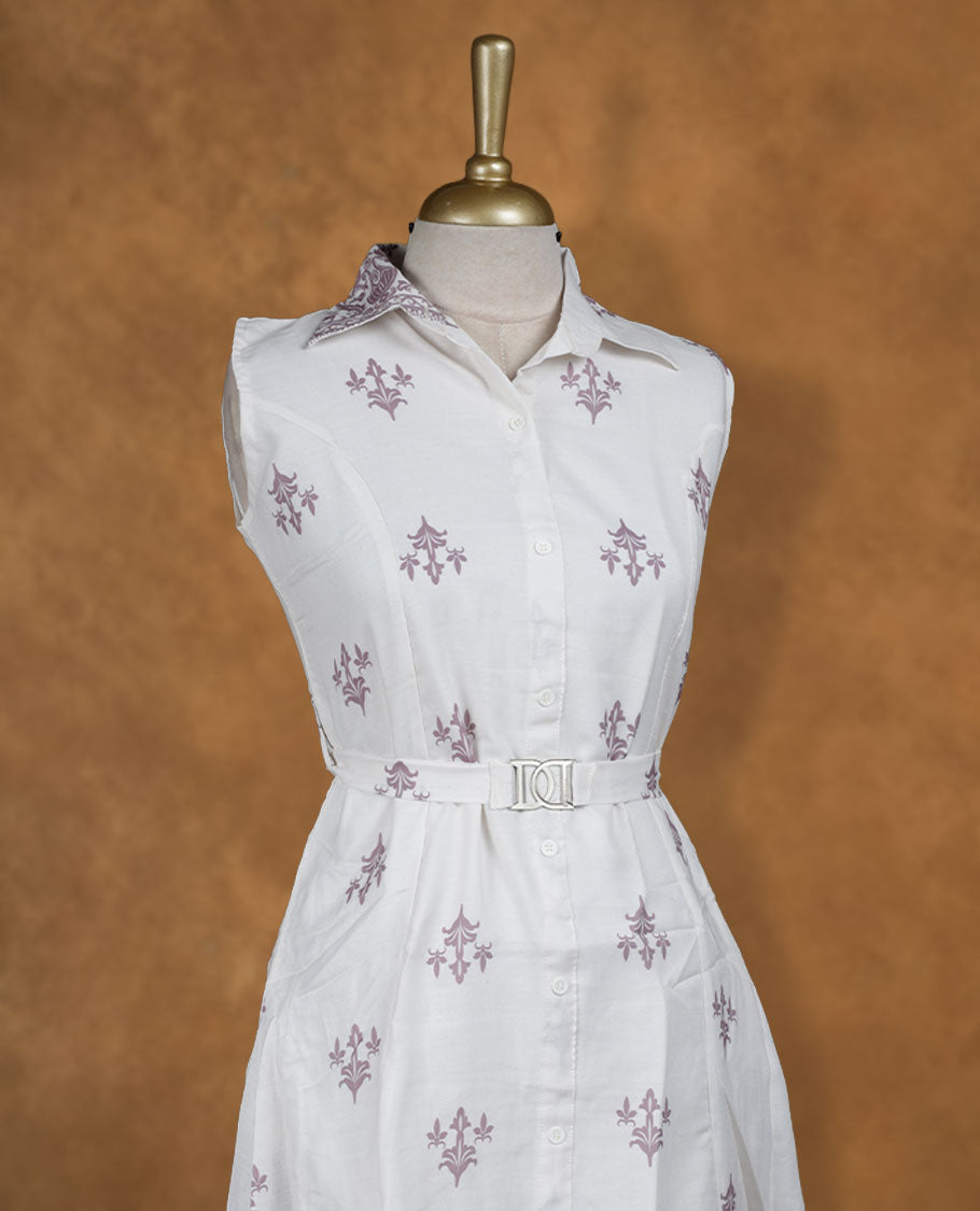 White sleeveless shirt dress with subtle mauve ethnic motifs, front button placket, matching waist belt with metal buckle, and ornate border print at hem.