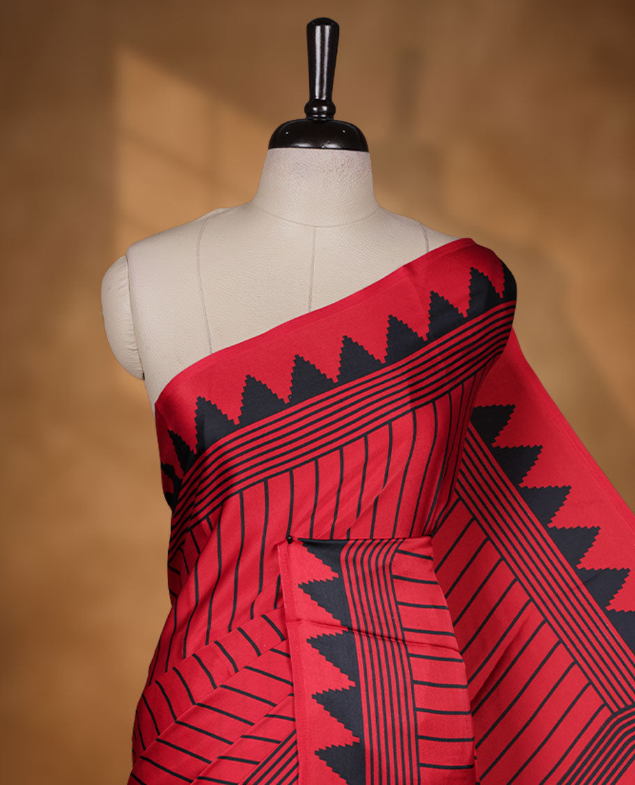 Red colour semi modal saree featuring black colour geometric borders and fine stripe detailing, finished with an oversized circular motif on the pallu, paired with a matching printed blouse.